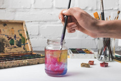 艺术家在工作场所将油漆刷放入玻璃罐中的裁剪镜头