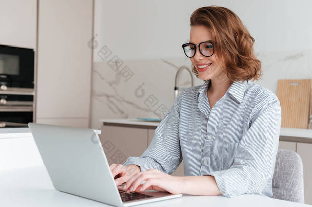 优雅的微笑的女人在眼镜和<strong>条纹衬衫</strong>使用笔记本电脑 