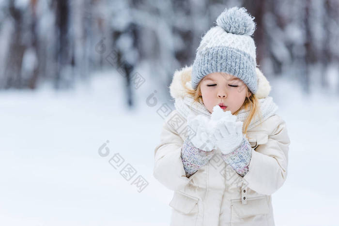 在冬季公园手里吹雪球的可爱的孩子画像