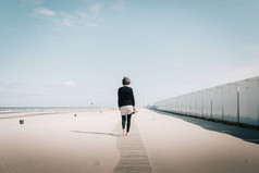 年轻的女人在阳光下的沙滩上漫步, 带着蓝天