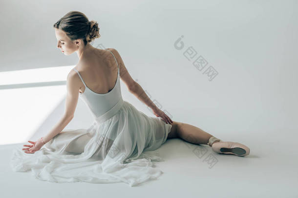 芭蕾舞女演员坐在白色礼服和芭蕾舞鞋后视图