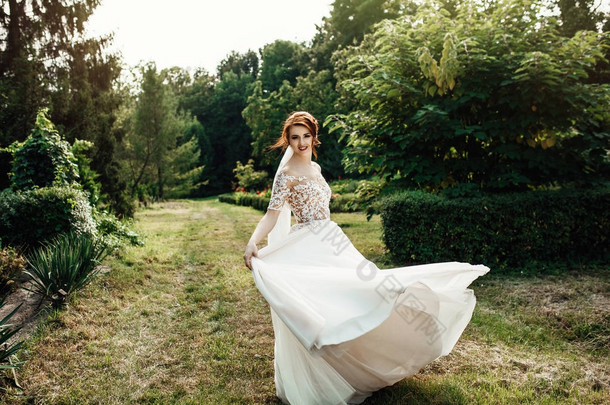 美丽的新娘穿着白色豪华的礼服站在绿色花园