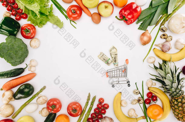 在白色的蔬菜和水果之间的小购物车的顶部视图
