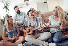 一群朋友在家里的客厅里玩得很开心。快乐的年轻人用吉他演奏音乐, 一起唱歌和欢笑 .
