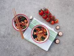 传统的亚洲炒锅用鸡肉、蔬菜和筷子在水泥石背景五颜六色的碗中。美味泰国晚餐.