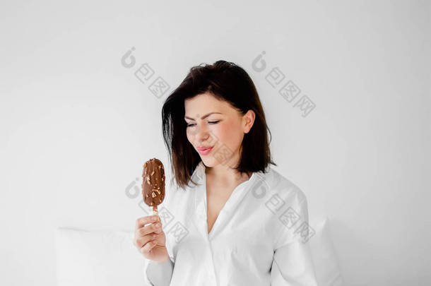 美丽的年轻的黑发妇女有清爽的冰淇淋。快乐的微笑的女孩有乐趣和吃冰淇淋在白色的房间。复制文本空间