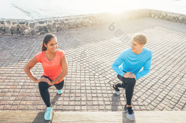慢跑夫妇舒展腿, 而微笑对彼此-运动的年轻人训练在日落室外-体育, 关系, 健康生活方式概念