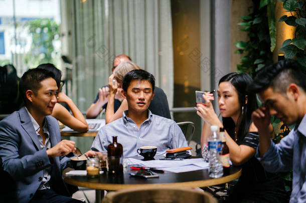  一群年轻精力充沛的亚裔同事围坐在桌旁, 进行着轻松的商务<strong>讨论</strong>。他们一边笑一边笑, 因为他们说话和交谈。.