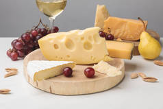 不同类型的乳酪在木板, 酒玻璃, 果子和杏仁在灰色