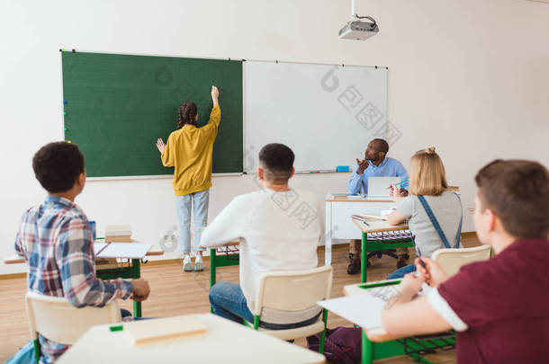 学生在粉笔板上的背观与教师坐在教室里的同学 
