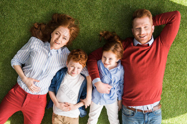 幸福的红发家庭与两个孩子躺在草地上, 微笑着在相机的顶部视图