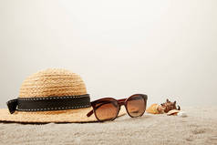 灰色背景下沙滩上草帽、太阳镜和贝壳的特写