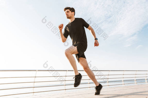 英俊的年轻运动员在沙滩上奔跑的形象听音乐用耳机.