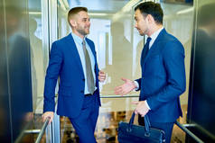 两位成功商人的肖像在现代办公楼中愉快地坐着玻璃电梯聊天