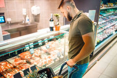 男人在杂货店里选择新鲜冰鲜的肉.男人在市场上购买冷冻食品，顾客在超级市场购买商品
