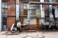 一个陈旧的生锈的危险的通风系统在一个过时的金属回收厂。一家工厂的五颜六色的砖墙倒塌了，工厂的窗户肮脏得可怕，后面有一扇门.