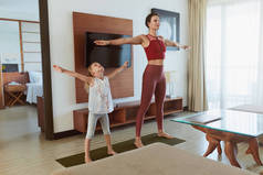 家庭健身在家里。母亲和女儿在客厅里锻炼。小女孩和年轻女子在草地上练习。积极生活方式的体育常规.