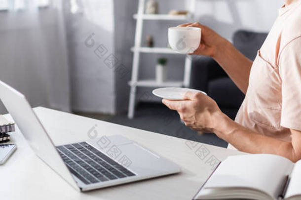 在家里，人们在笔记本电脑和文具旁边拿着杯子和茶托的全景照片，在网上获得了灵感