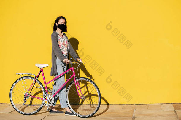身着<strong>粉色</strong>复古自行车、头戴防护面罩、走在五颜六色的黄色<strong>墙</strong>壁前的小女孩，拥有积极的生活方式和可持续的行动能力，抄袭文字空间