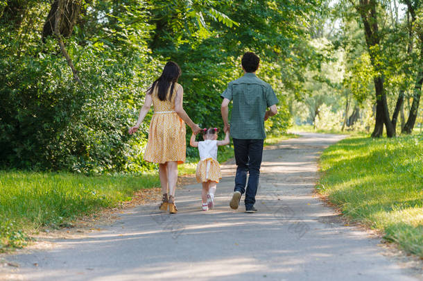 回顾快乐的家庭手牵手走在小径上，在美丽的绿色公园里度过时光的<strong>情景</strong>.