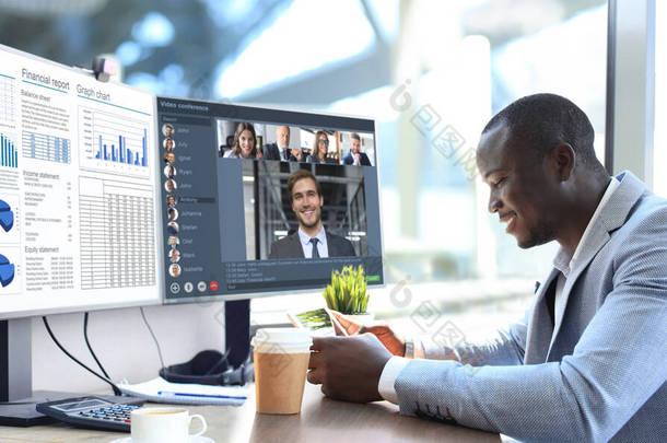 非裔美国商人在视频会议上与他的同事交谈。利用个人电脑在办公室工作的多族裔商业团队，讨论他们公司的财务报告.