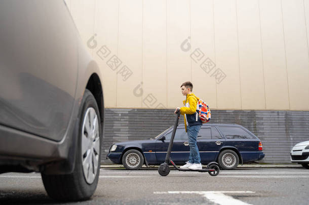 一个英俊的少年，背着背包骑<strong>电动车</strong>沿着城市街道走下去