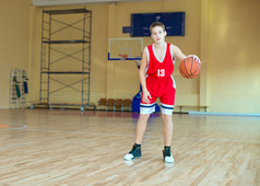 球在他的手，红色的制服的篮球运动员。在健身房里练习打篮球