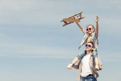 父亲和女儿白天在公园里玩纸板玩具飞机。友好家庭的概念。人们在户外玩得很开心在蓝天的背景上拍摄的图片.
