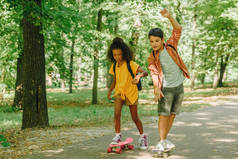 两个多元文化的小学生在阳光明媚的公园里玩滑板