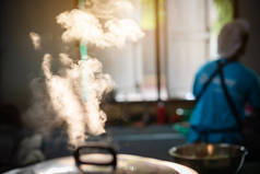 当厨师工作时，一个巨大的电饭锅在食堂里沸腾，其晨光反射出大量的蒸汽.