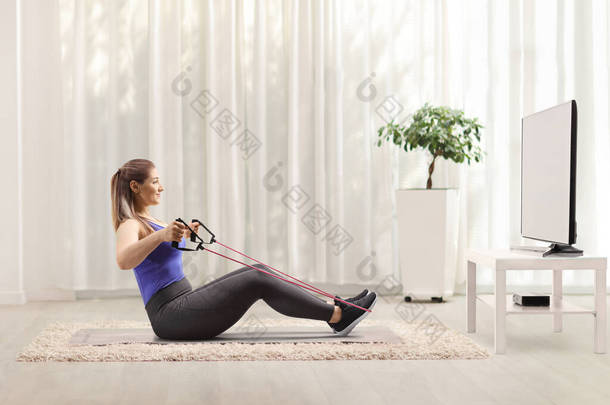 一个女人坐在地板上，在家里的电视机前和一个抵抗乐队一起锻炼