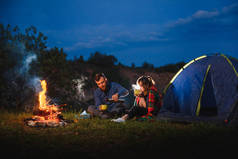 晚上在山上露营。一对快乐的夫妇坐在篝火边，点燃着旅游帐篷。背景巨大的巨石森林和夜空.