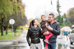 在遮阳伞下的女儿一家人漫步在雨天.