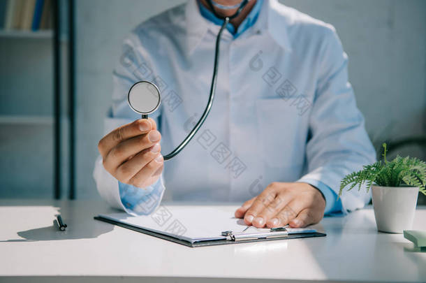 医生坐在办公桌前举着听诊器的剪影