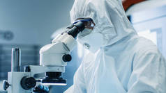显微镜下的工程师/技术员/科学家检查组件的特写。他在工作项目时穿着无菌工作服和防护眼镜。.