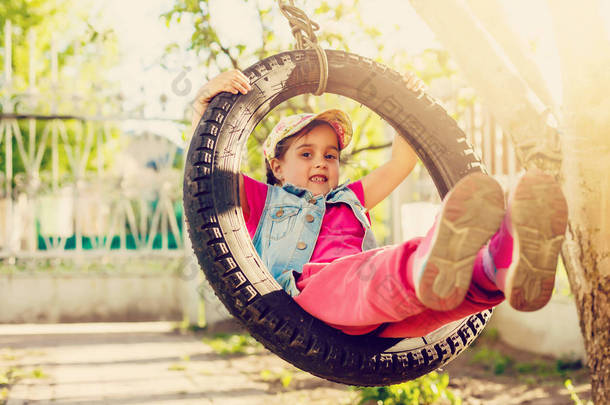 快乐的小女孩在绿色花园的轮胎<strong>摆动摆动</strong> 