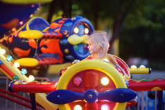 小男孩在公园里享受景点的乐趣。夏天晚上，孩子骑着旋转木马转来转去。景点，飞机，汽车，照明，乐趣...