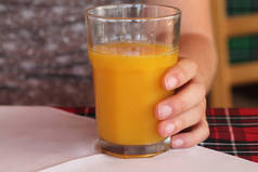 一杯鲜榨橙汁的特写镜头站在桌子上，左手拿着 