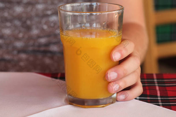 一杯鲜榨橙汁的特写镜头站在桌子上，左手拿着 