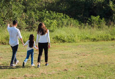 在一个阳光明媚的夏日，快乐的亚洲年轻家庭的父亲、母亲和孩子们，一起在外面的绿树成荫的自然公园里散步，享受着户外运动的快乐
