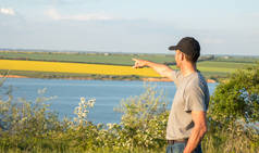 在帽子的农村男子欣赏日落的湖和黄土地