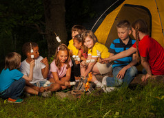 露营者坐在一起在篝火附近的棉花糖