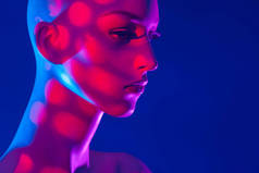 蓝色背景的人体模特。 人体模特的脸部分被粉色的光照亮了。 商店橱窗的女模特。 化妆的女娃娃.