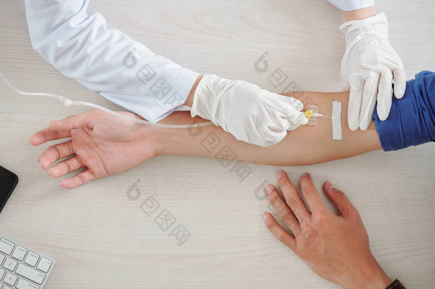 男病人在医院接受输液治疗，医疗护士在手臂静脉中插入静脉导管