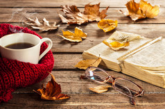 热咖啡、古董书、玻璃杯和木头上的秋叶