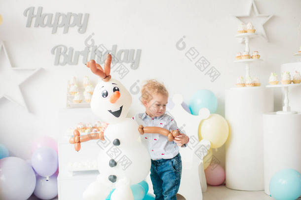 在孩子们的聚会上，一个带着气球和蛋糕的金发碧眼的小男孩在生日那天很可爱。孩子们的派对气球；气球