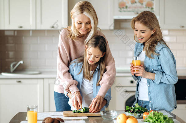 <strong>三代</strong>女人在厨房呆在一起，奶奶教孙女切沙拉，妈妈笑着看着旁边的果汁