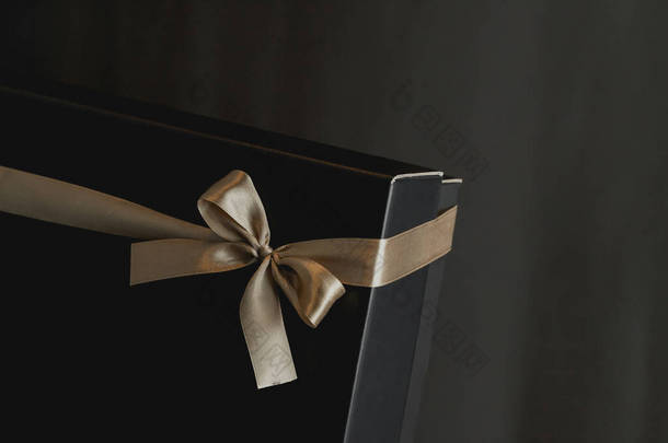 黑色<strong>礼品</strong>盒的特写镜头，带着优雅的金色缎带，背景是深色的豪华蝴蝶结。带有文字位置的<strong>礼品</strong>盒。生日,结婚周年礼物,<strong>礼品</strong>明信片.浪漫的气氛