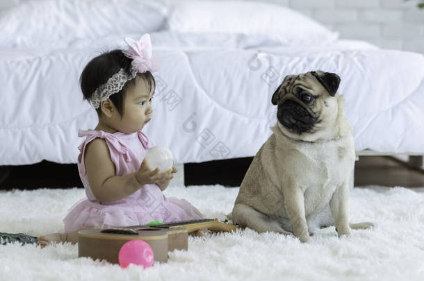 可爱可爱可爱的亚洲宝宝穿着白色的连衣裙坐在白色的床上微笑着，在舒适的卧室里快乐地玩耍，健康的宝宝概念