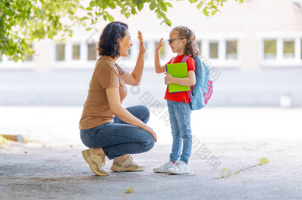 小学的父母和学生是紧密联系在一起的.背着背包的女人和女孩。开始上课。秋天的第一天.